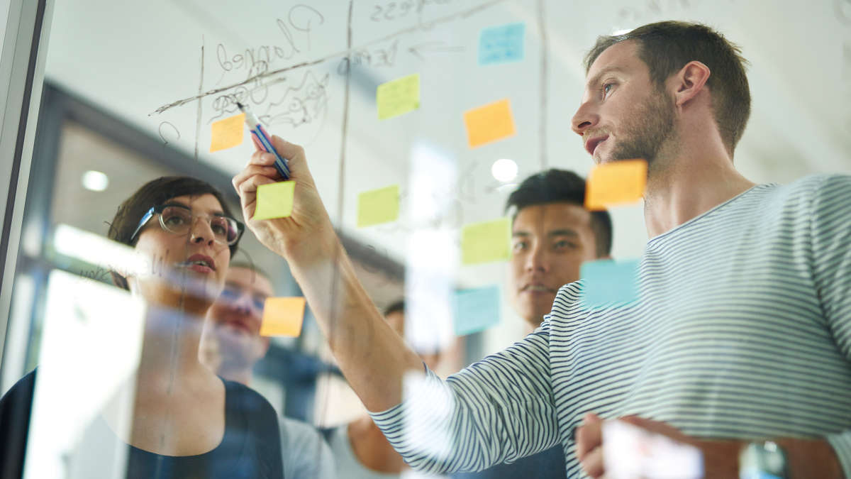 Three colleagues brainstorming behind a glass board with colorful sticky notes