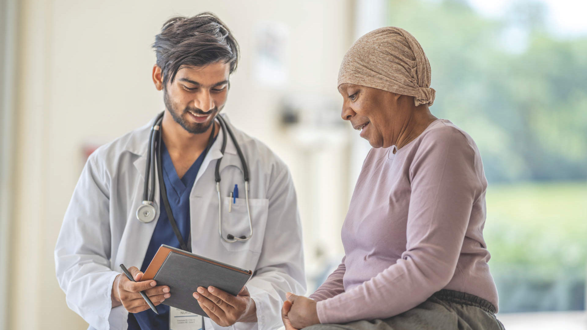 A male Oncologist of Middle Eastern decent sits with a senior patient as they discuss her medications